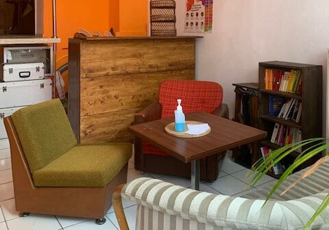 Bunte Sitzmöbel und ein Tisch stehen in einem Raum mit einem Bücherregal.