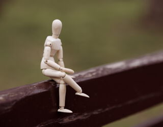 Eine Holzfigur sitzt auf einem Balken. Der Hintergrund ist verschwommen.