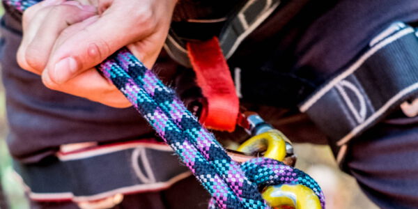 ein Bildausschnitt mit einer Person im Klettergurt mit einem Kletterseil in der Hand. Die Person seilt sich ab