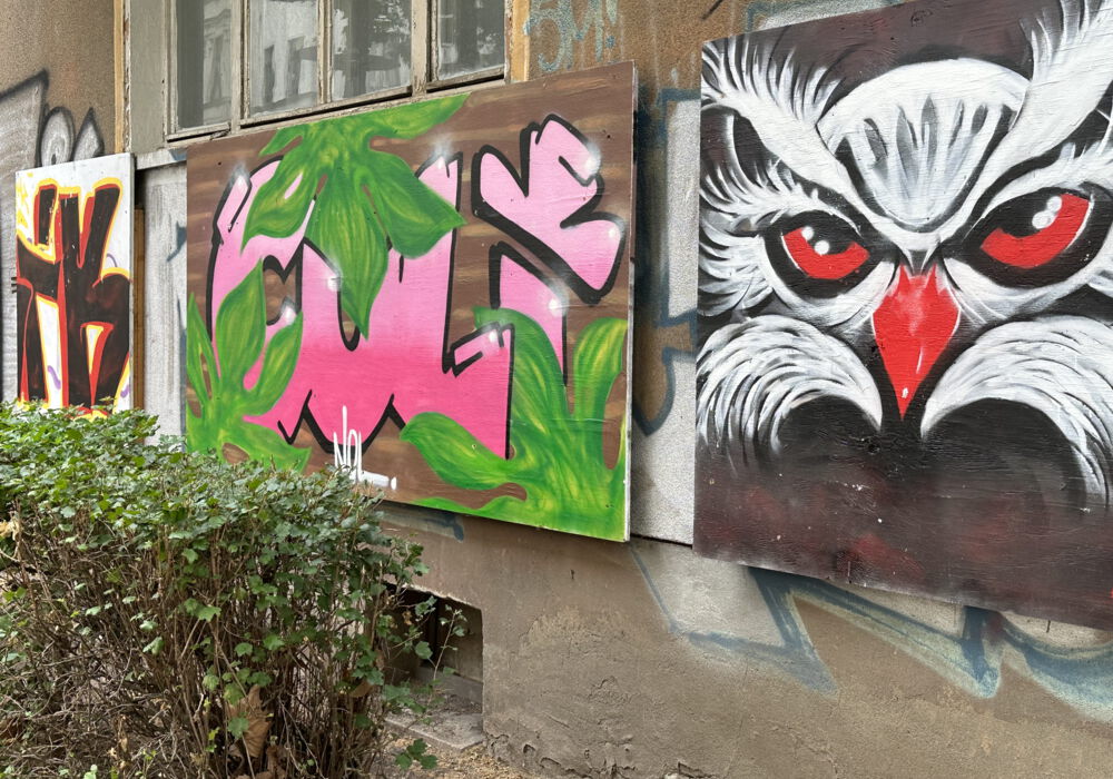mehrere Graffiti auf Holzplatten schmücken die Wand eines Hauses
