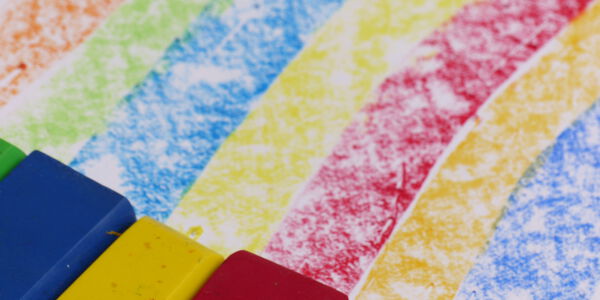 Sechs bunte Wachsstifte liegen auf einem bemalten Blatt Papier.
