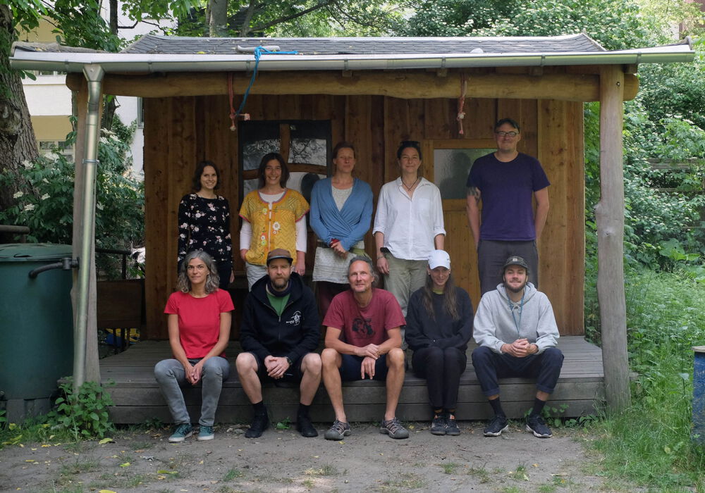 Zehn Personen stehen und sitzen gemeinsam vor einem Gartenhaus des Wohnprojektes.