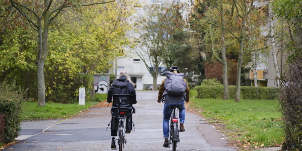 zwei Personen von hinten auf ihren Fahrrädern sind in einem Wohngebiet mit grünen Bäumen unterwegs