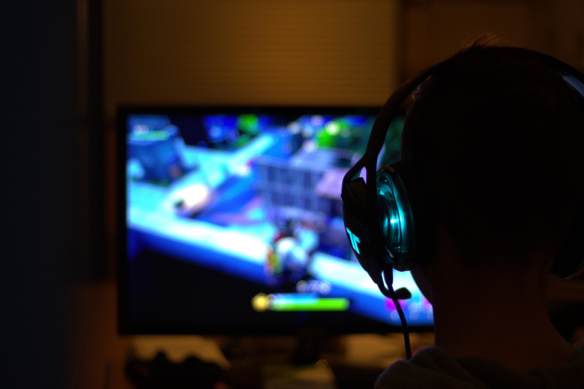 Im Vordergrund ist ein Kopf von hinten zu sehen. Die Person hat Kopfhörer aus. Die Person sitz vor einem Computerbildschirm.