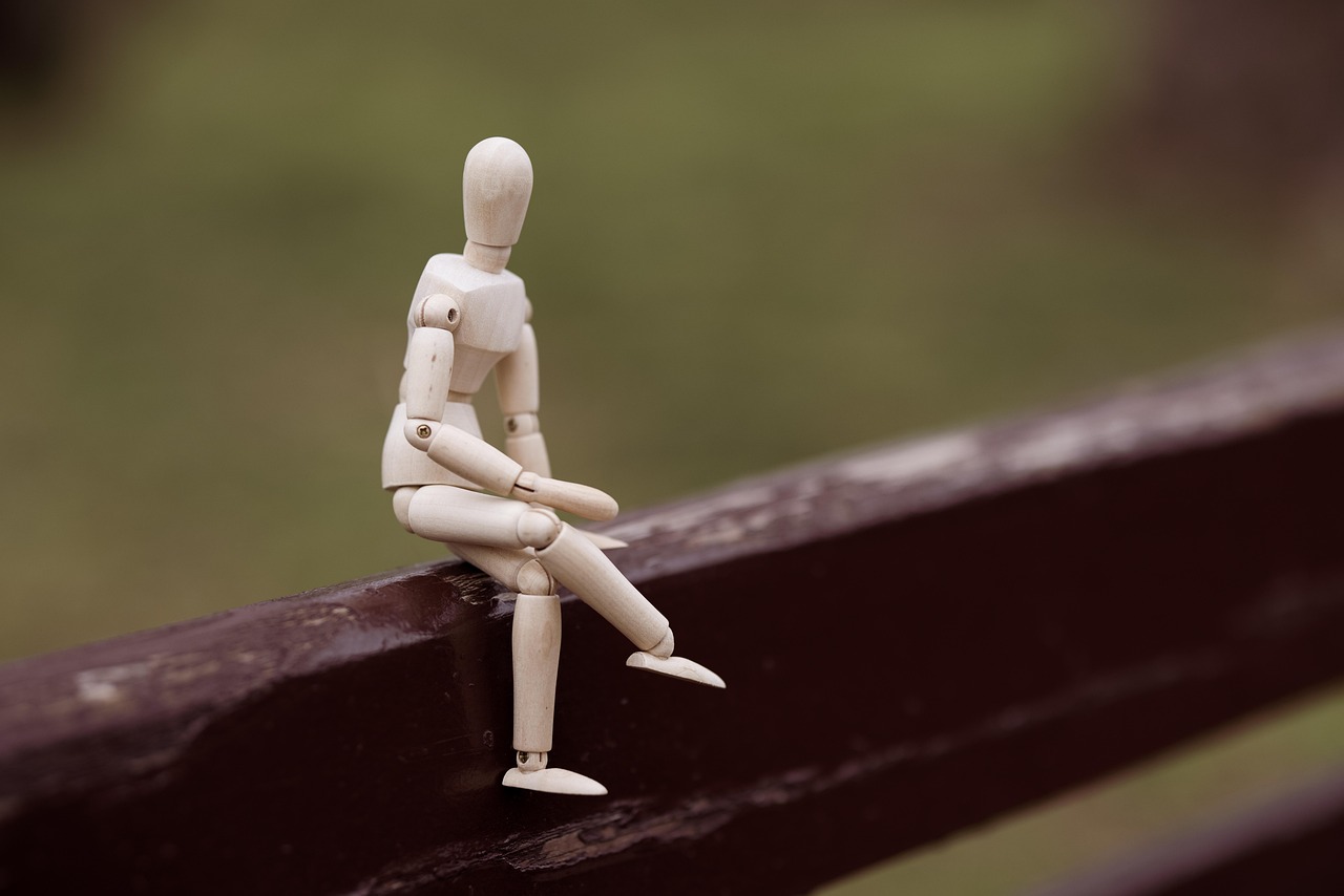 Eine Holzfigur sitzt auf einem Balken. Der Hintergrund ist verschwommen.
